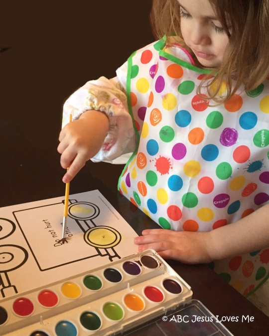 Little girl painting with watercolors the ABCJesusLovesMe worksheet.