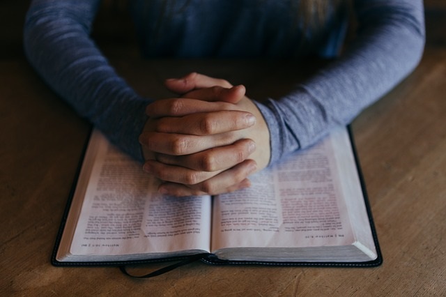 Women's hands folder over an opened Bible.