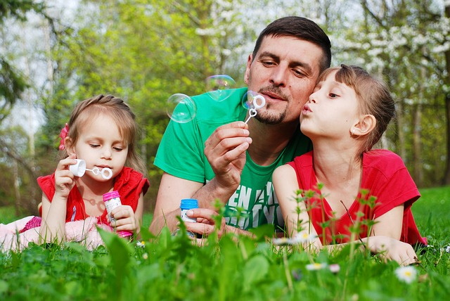 Dad blowing dandelion with his daughters