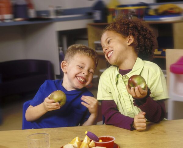 Boy and girl laughing and eating apples.