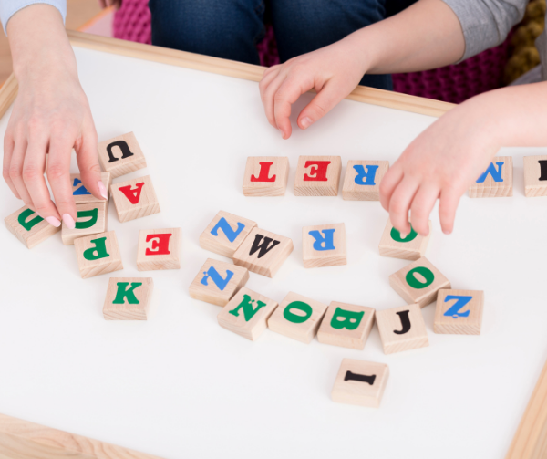 Child and Adult Sitting a table with Letter Blocks
