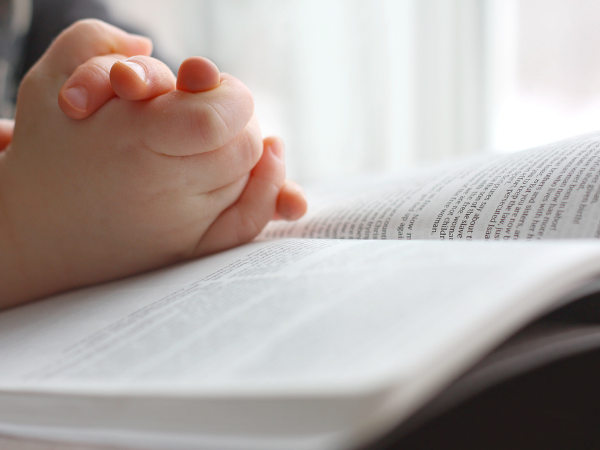 Child folding hands on a Bible.