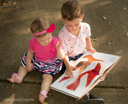 Young girl and boy look at a book.