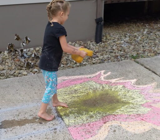 Child playing with water and sidewalk chalk.