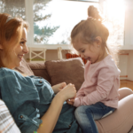 Child sitting on her mom's lap. They are holding hands.