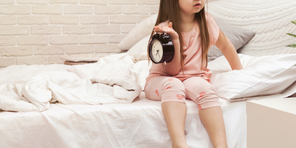 Child in bed holding an alarm clock.