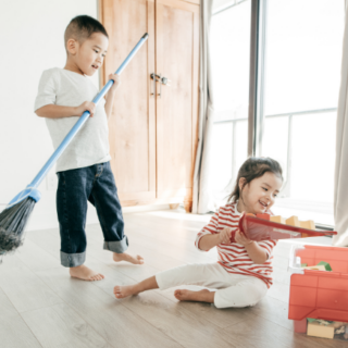 Boy and girl picking up blocks with a broom and dustpan.