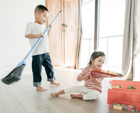 A boy and girl picking up blocks with a broom and dustpan.