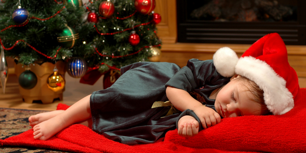 Little girl asleep in front of a Christmas tree.