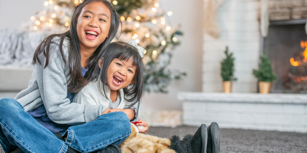 Two happy, young girls sitting in front of a Christmas tree.