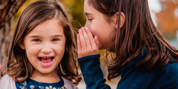 A girl whispering in another girl's ear.