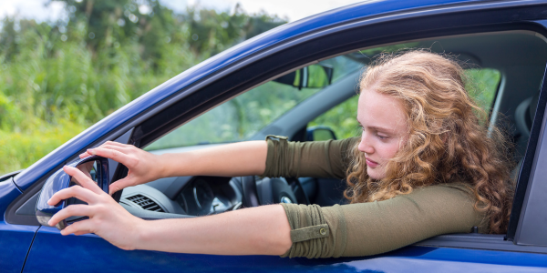 Woman looking in side mirror of car.