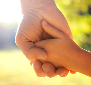 Adult and child holding hands outside.