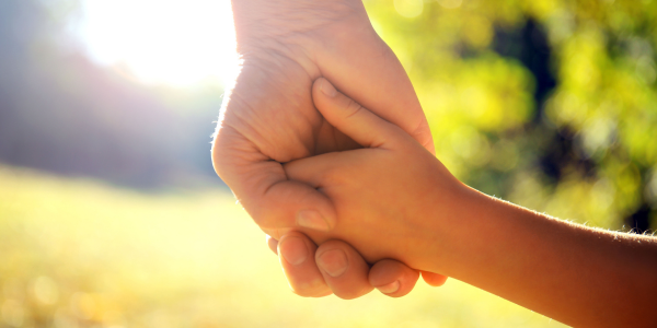 Adult and child holding hands outside.