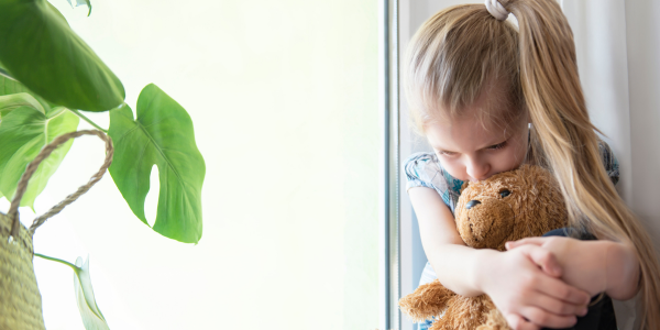 A sad girl hugging her teddy bear.