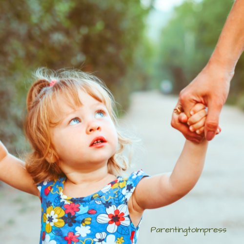 A little girl walking on a path while holding mom's hands.
