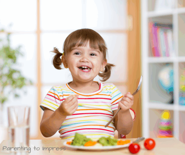 a little girl smiling, eating her dinner