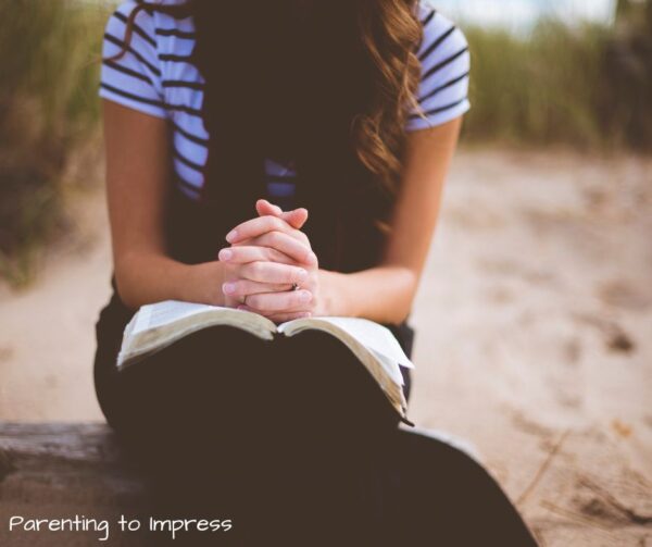 a mom with open bible, hands folded in prayer