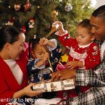 2 parents and 2 children in front of the christmas tree, smiling, opening gifts