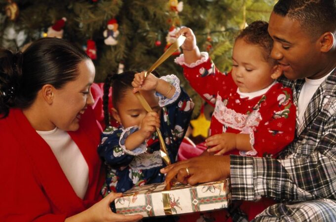 2 parents and 2 children in front of the christmas tree, smiling, opening gifts