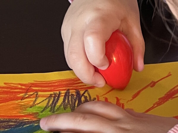 Child coloring with an egg crayon.