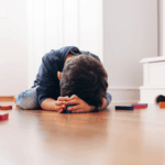 A tired child, lying on the floor with blocks.